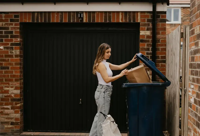 Homeowner putting a cardboard box into an outdoor bin beside a garage